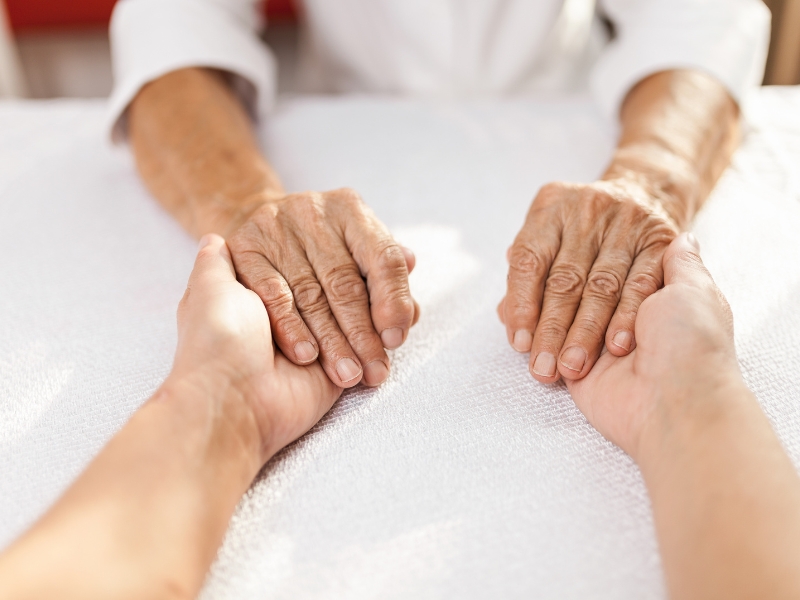 carer support dementia – caregiver holding elderly person’s hands on white table showing compassion and connection