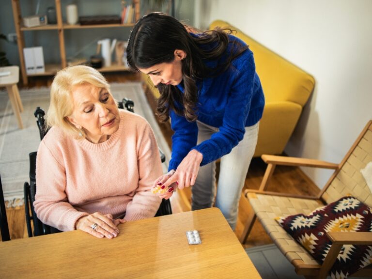 Caregiver helping elderly woman in wheelchair with medication, demonstrating compassionate elderly support at home.