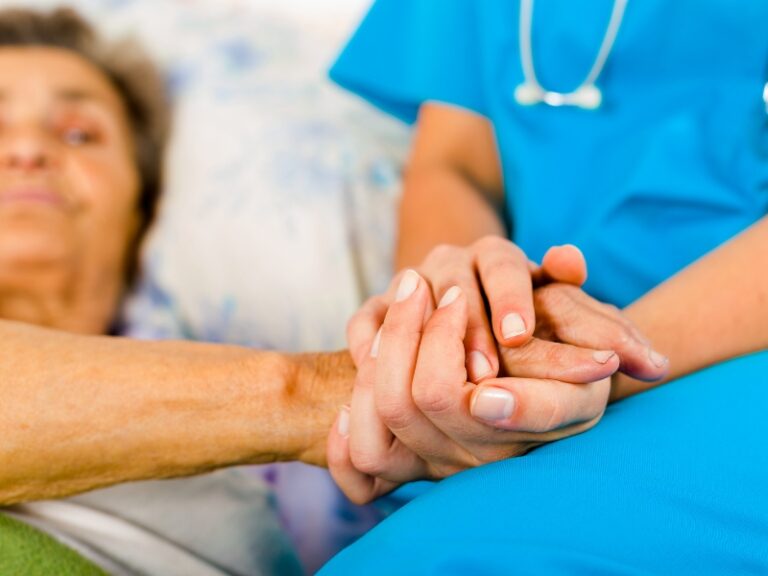 Caregiver holding elderly patient’s hand with compassion, symbolising gentle assistance in personal care tasks.