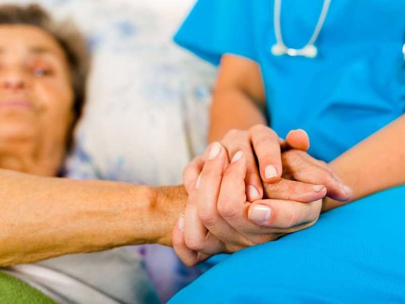 Caregiver holding elderly patient’s hand with compassion, symbolising gentle assistance in personal care tasks.