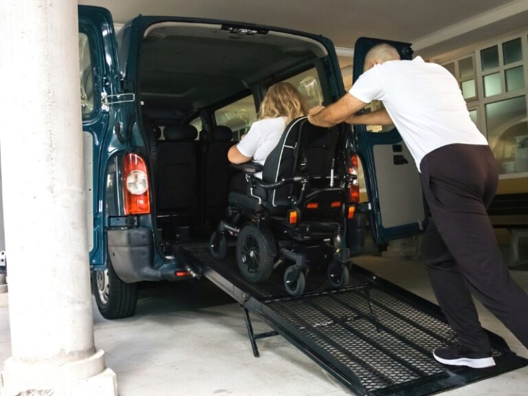 Caregiver helping woman in wheelchair onto van ramp, providing assistance with travel transport arrangements.
